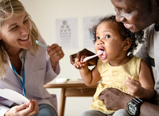 Dentist teaching a little girl how to brush her teeth