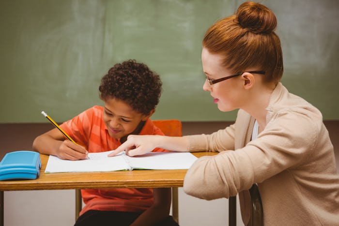 Portrait of teacher assisting little boy with homework in the classroom