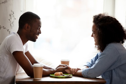 Happy multiracial couple holding hands, enjoying date in cafe, smiling African American boyfriend lo...