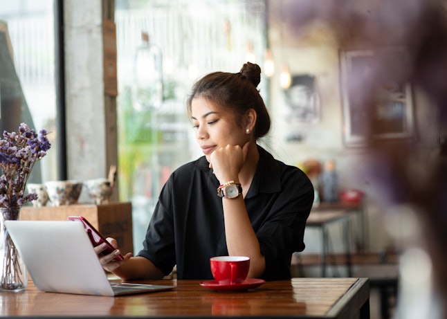 Asian woman working in cafe and using smart phone.