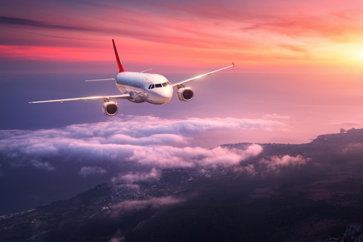 Passenger airplane. Landscape with big white airplane is flying in the red sky over the clouds and s...