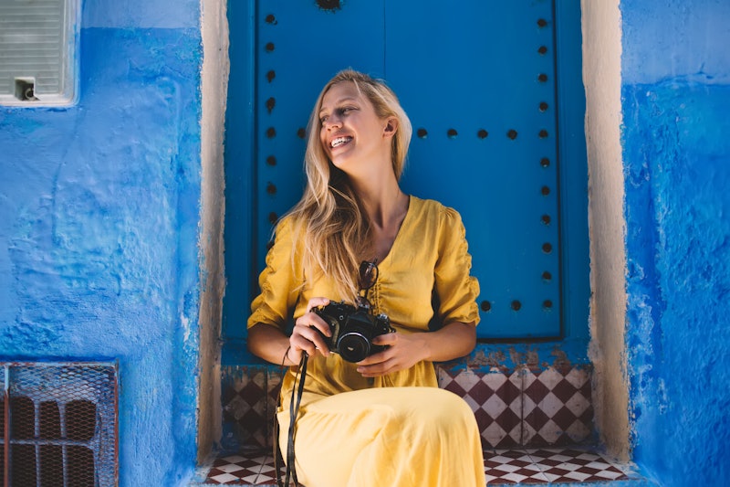 Excited female tourist with retro equipment in hands resting near oriental blue doors in Morocco and...