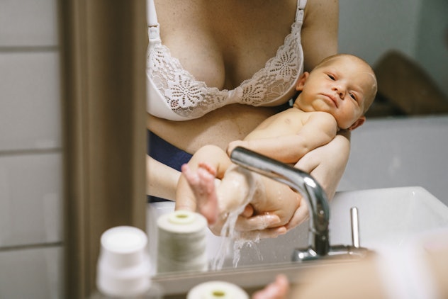 Bathing a newborn home. Mom is holding a baby in the bathroom and washes it under a stream of water ...