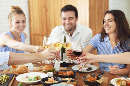 Hands with white wine toasting over served table with food. Friendship and happiness  concept