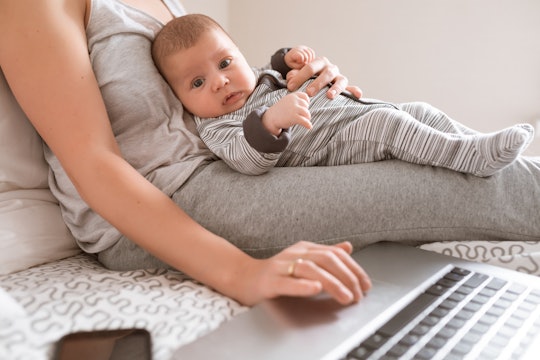 Young mother in home office with laptop and her newborn baby.