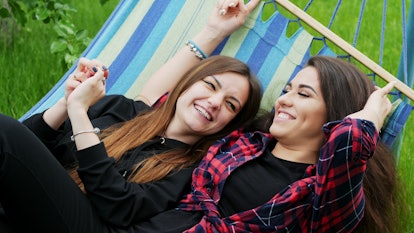 Lesbian girlfriends lie in hammock in garden. Two lesbians woman hug and laugh, lgbt concept