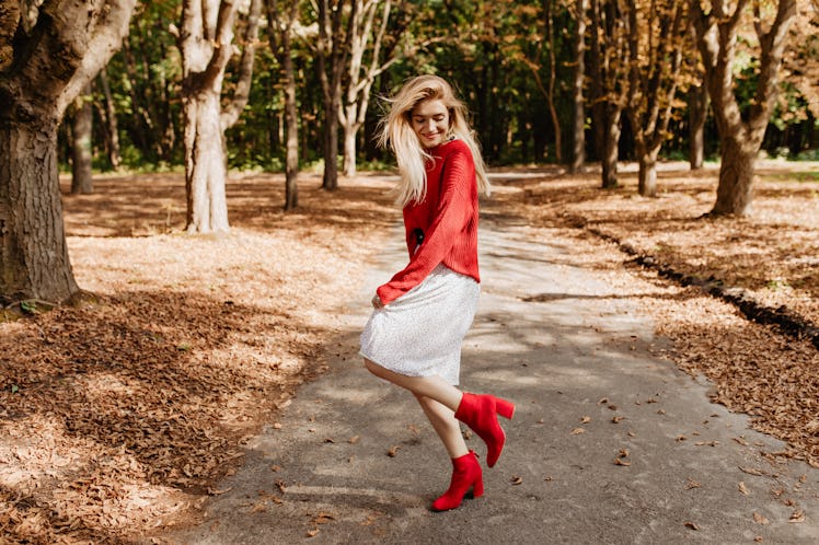 Smiling young blonde woman having fun in autumn park. Dancing in stylish red shoes and white dress.