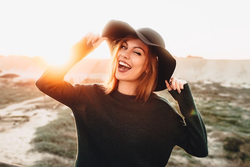 Portrait of beautiful blonde young woman in glasses and holding hat and winking on the beach with su...