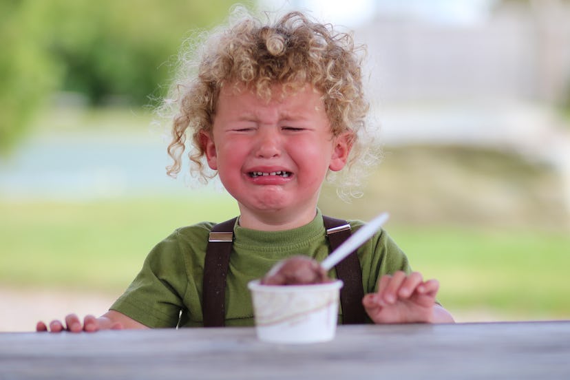 A little boy is upset, holding chocolate ice cream. The young child is visibly mad or sad.