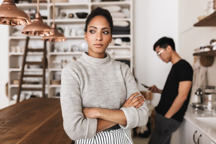 Beautiful serious african american woman holding hands together angrily looking aside with asian man...