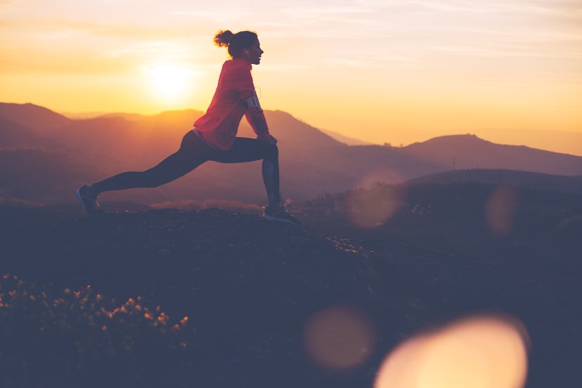 Silhouette of athletic girl doing stretching after a great jog in the mountains at sunset. Sport tig...