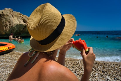 Woman female girl with hat holding and eating a slice piece of colorful red green watermelon at the ...