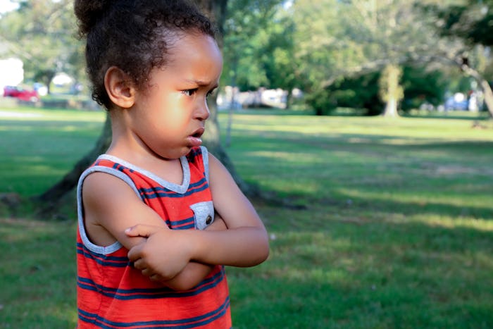 A young African American boy is unhappy at the park. His arms are crossed and his expressions shows ...