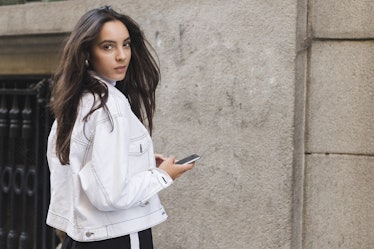 Young woman in jacket looking over shoulder holding the mobile phone in hand