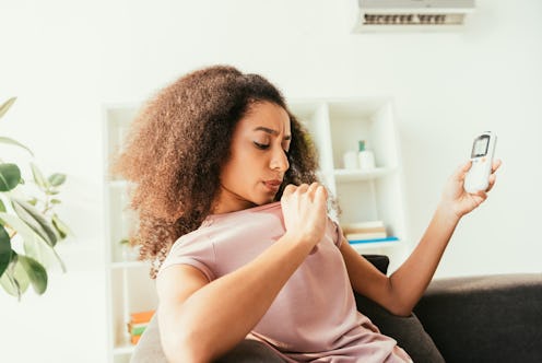 young african american woman in sweaty shirt holding air conditioner remote controller