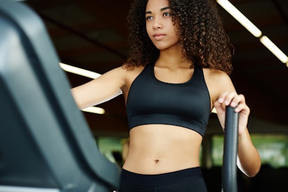 Young fit woman dressed in sports bra working out on stepping machine in gym