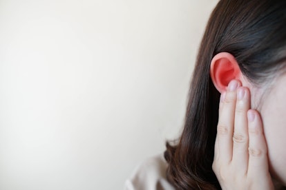 Young woman suffering from ear pain and tinnitus. Cause of earache includes otitis, earwax buildup, ...