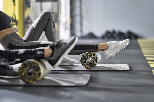 Nice girls are training with black-yellow foam rollers on the gray mats in the gym. They are wearing...