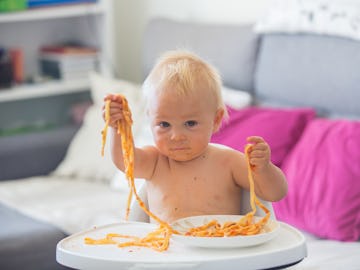 Adorable little baby one year old eating pasta indoor. Funny toddler child with spaghetti. Cute kid ...