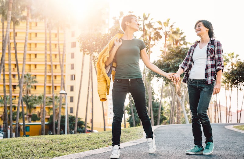 Happy lesbian couple having fun dating outdoor - Young gay women walking and holding hands outside -...