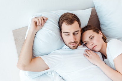 pensive couple in white t-shirts lying on bed and looking away