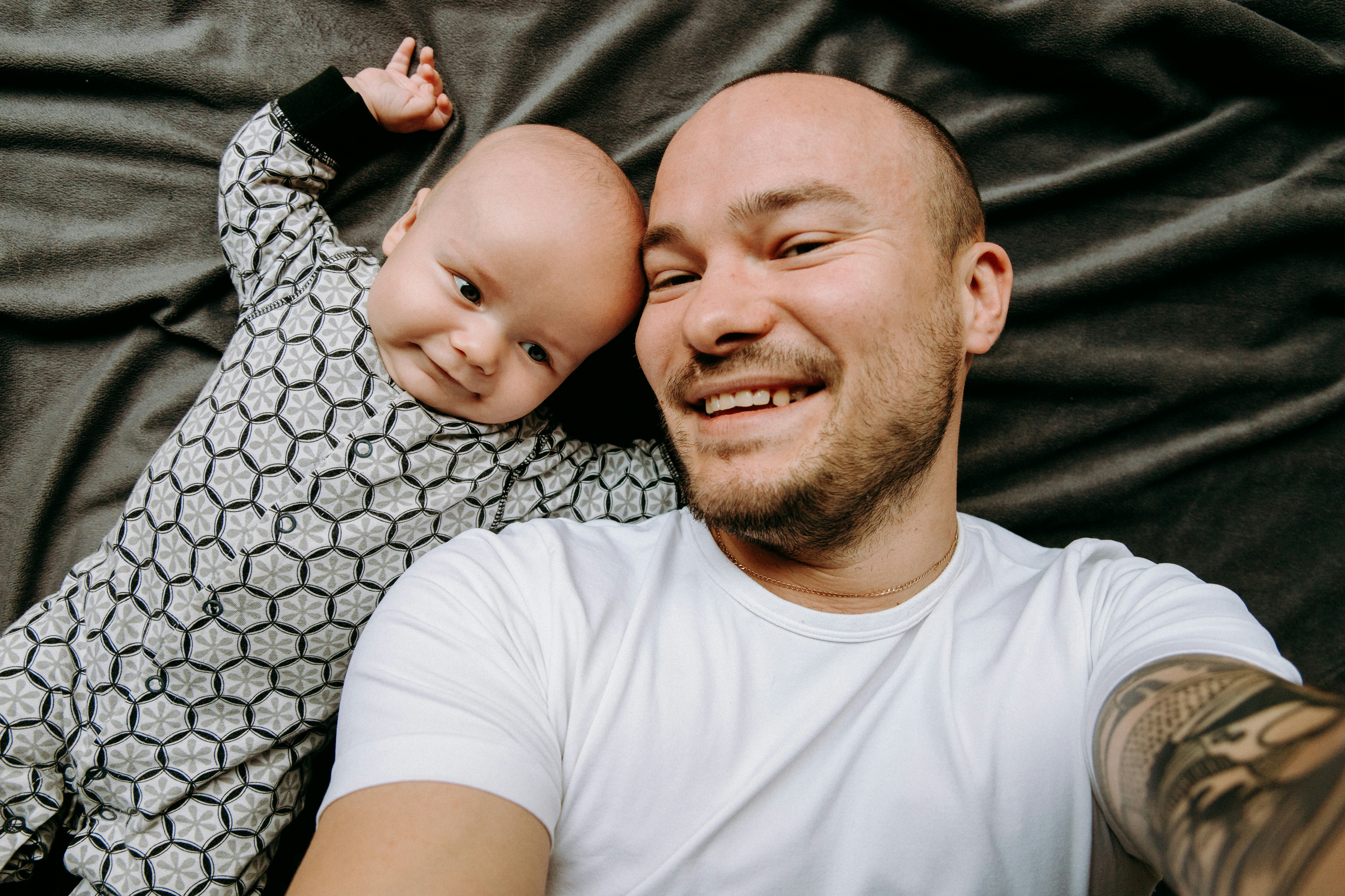 dad and baby take a selfie. They are smiling on a gray background.