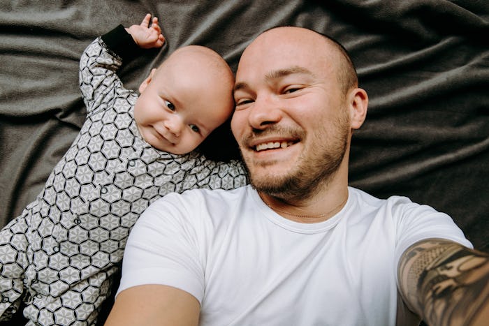 dad and baby take a selfie. They are smiling on a gray background.