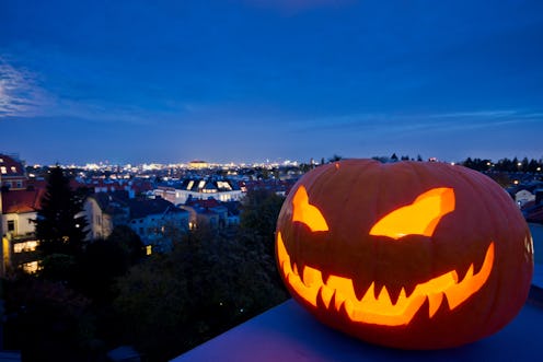 Halloween jack-o'-lantern with pumpkin face creates scary evening mood. Clear view to the cityscape ...
