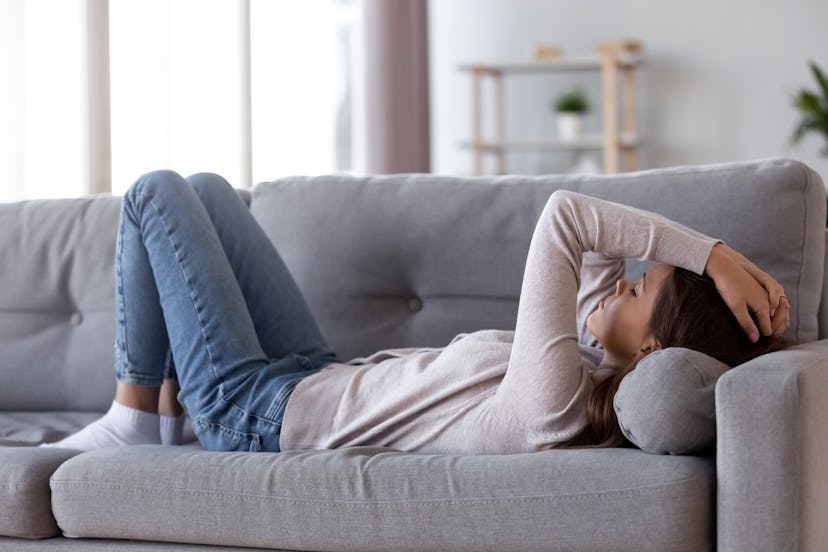 Sad depressed young woman lying on couch at home feeling headache fatigue loneliness, upset tired si...