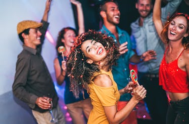 Happy friends doing party at night club - Young woman having fun with group of mates eating candy lo...