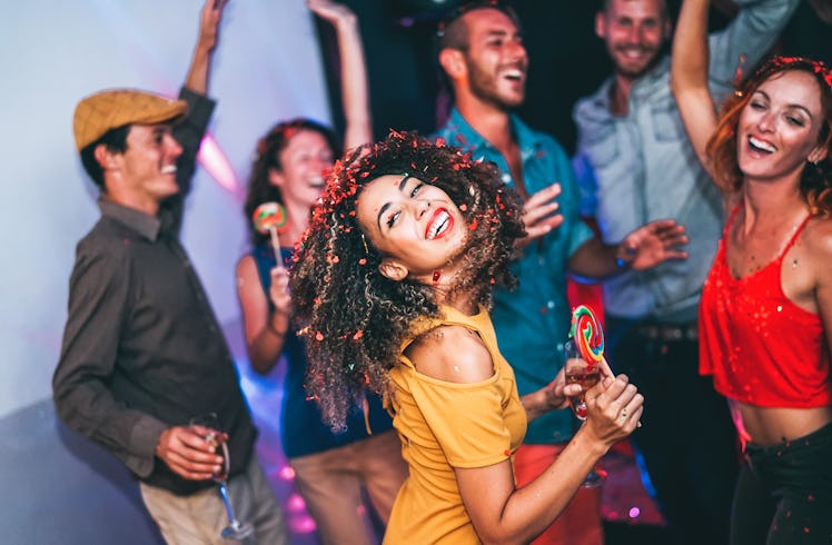 Happy friends doing party at night club - Young woman having fun with group of mates eating candy lo...