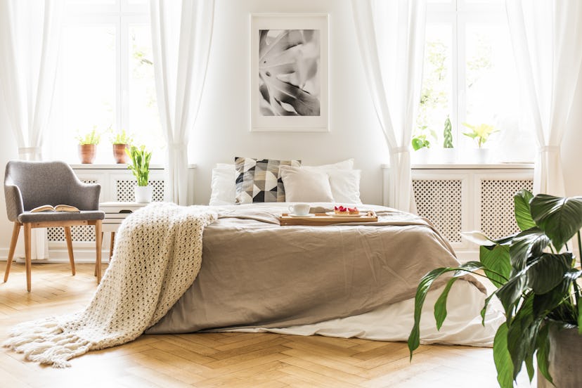 Open book on a gray, wooden armchair by a cozy bed with breakfast tray in a stylish bedroom interior...