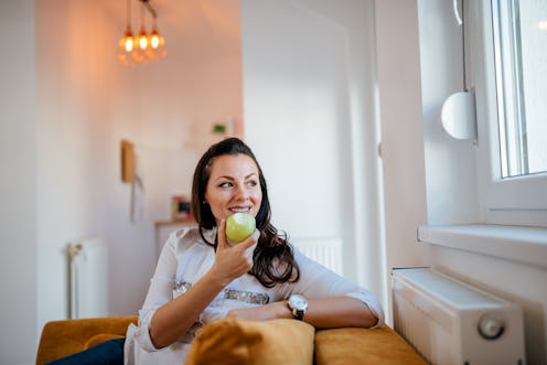Charming woman eating apple and looking through window at home.