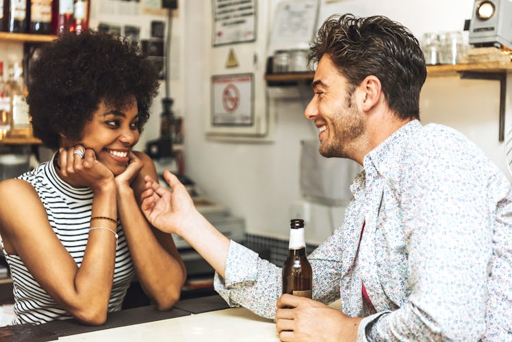 Young man holding bottle of beer and flirting with female bartender.