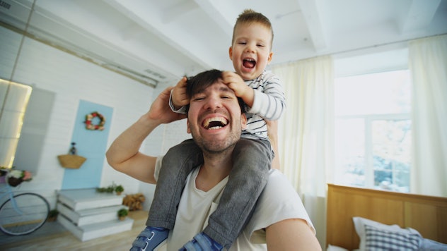 Happy father carrying his smiling son on neck and making selfie on smartphone in bedroom