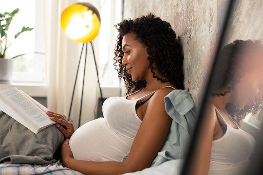 Interesting book. Happy expectant mother with a book reclining on a pillow in her bed.