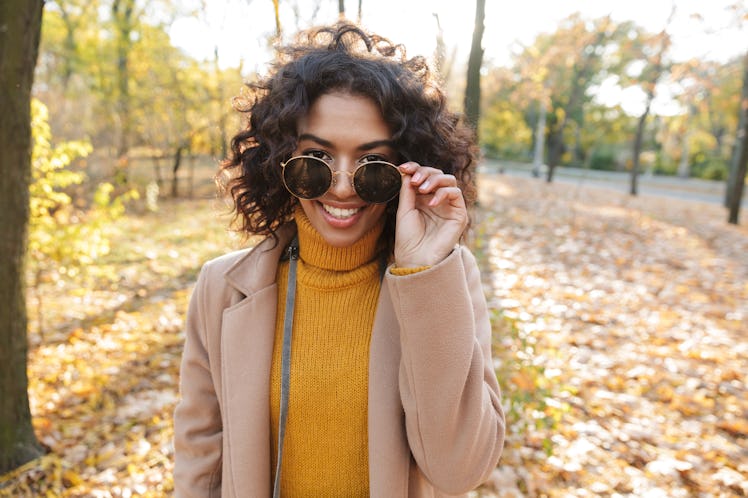 Smiling young african woman wearing autumn coat walking at the park