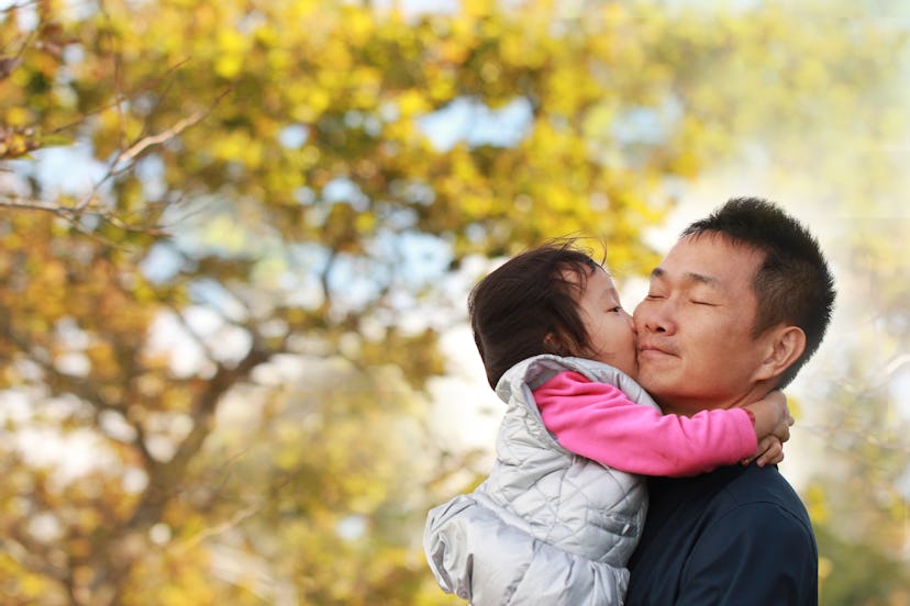 A Asian father holding and kissing baby girl before a golden tree on a meadow. Background for father...