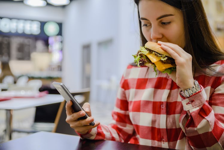 woman eat humburger in cafe while searfing the phone