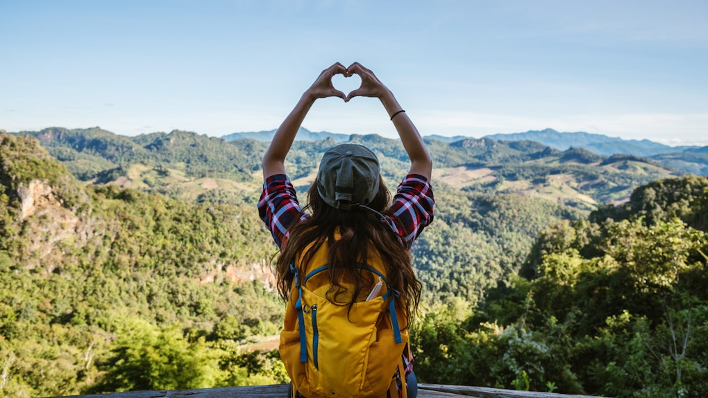 Young woman Tourists with backpacks Happy to travel She raised her hand to make a heart shape and enjoy the natural scenery on the mountain.