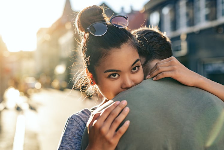 Young woman hugging her boyfriend while standing together on a city street in the late afternoon