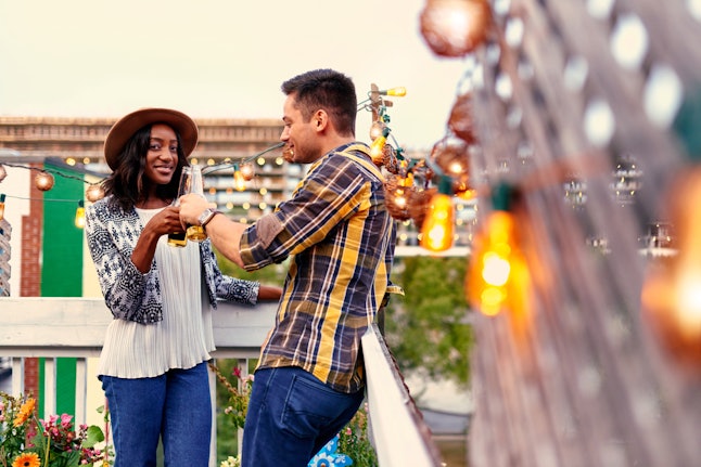 Multi-ethnic millennial couple flirting while having a drink on rooftop terrasse at sunset