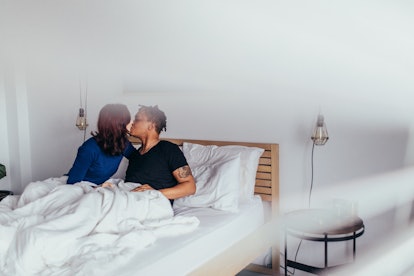 Romantic couple kissing in bed. Interracial man and woman sitting on bed and kissing each other.