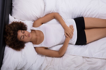 Young Woman Suffering From Stomach Pain Lying On Bed In Bedroom