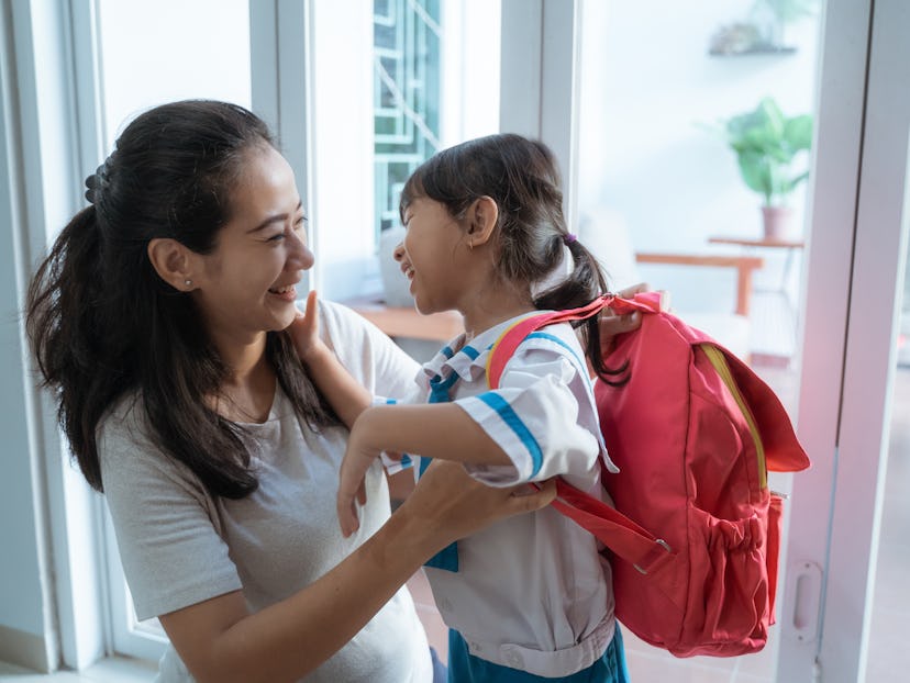 asian mother help her daughter to put the backpack on before going to school