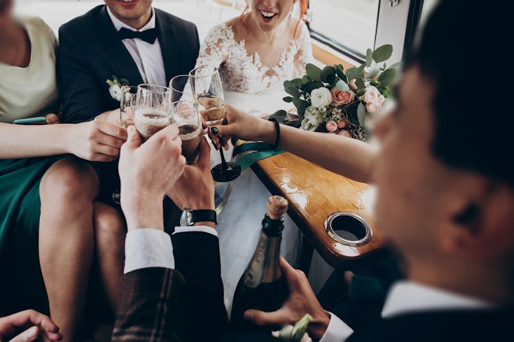 hands with glasses of champagne clinking, stylish happy bride and groom toasting laughing and having...