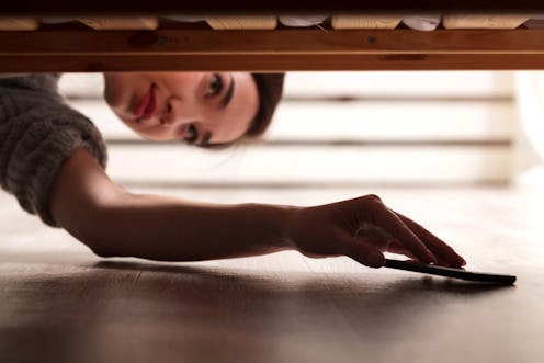 Closeup shot of girl who takes a smartphone from under the bed