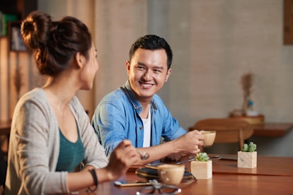 Portrait of young man and woman looking at each other and smiling, meeting in cafe for coffee
