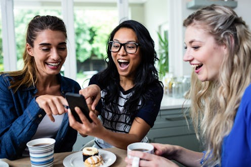 A group of friends sit around a kitchen table with coffee mugs looking at a phone.