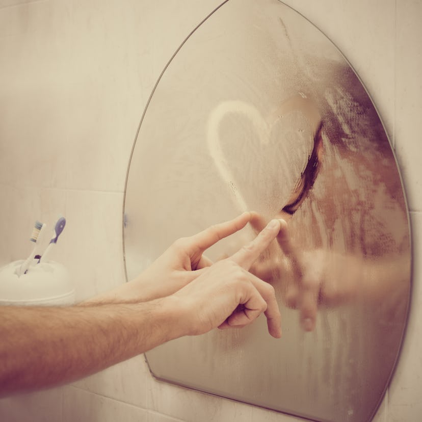 Couple in love drawing heart on misted mirror in bathroom, image with warm vintage toning